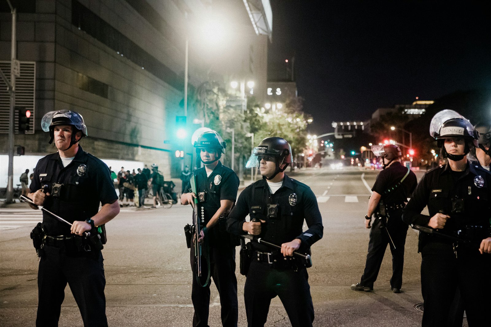 Line of police officers in riot helmets holding batons on a city street at night
